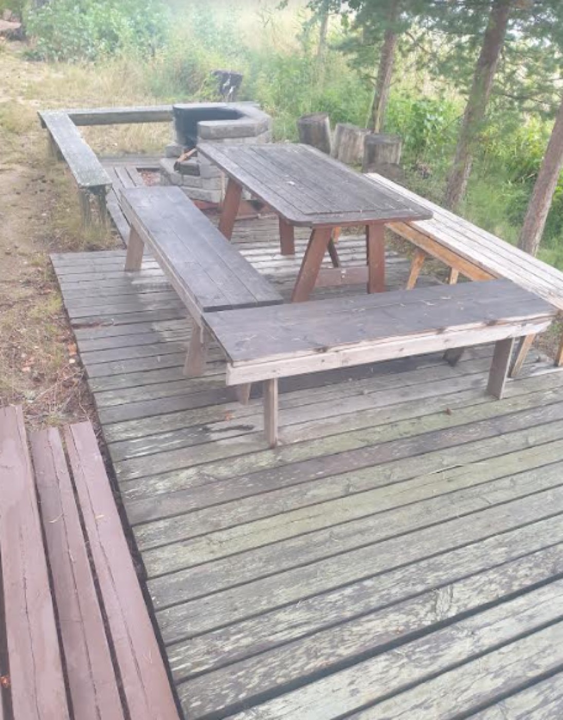 Grillipaikka, pöytä ja penkit rantasaunan terassitasanteella.